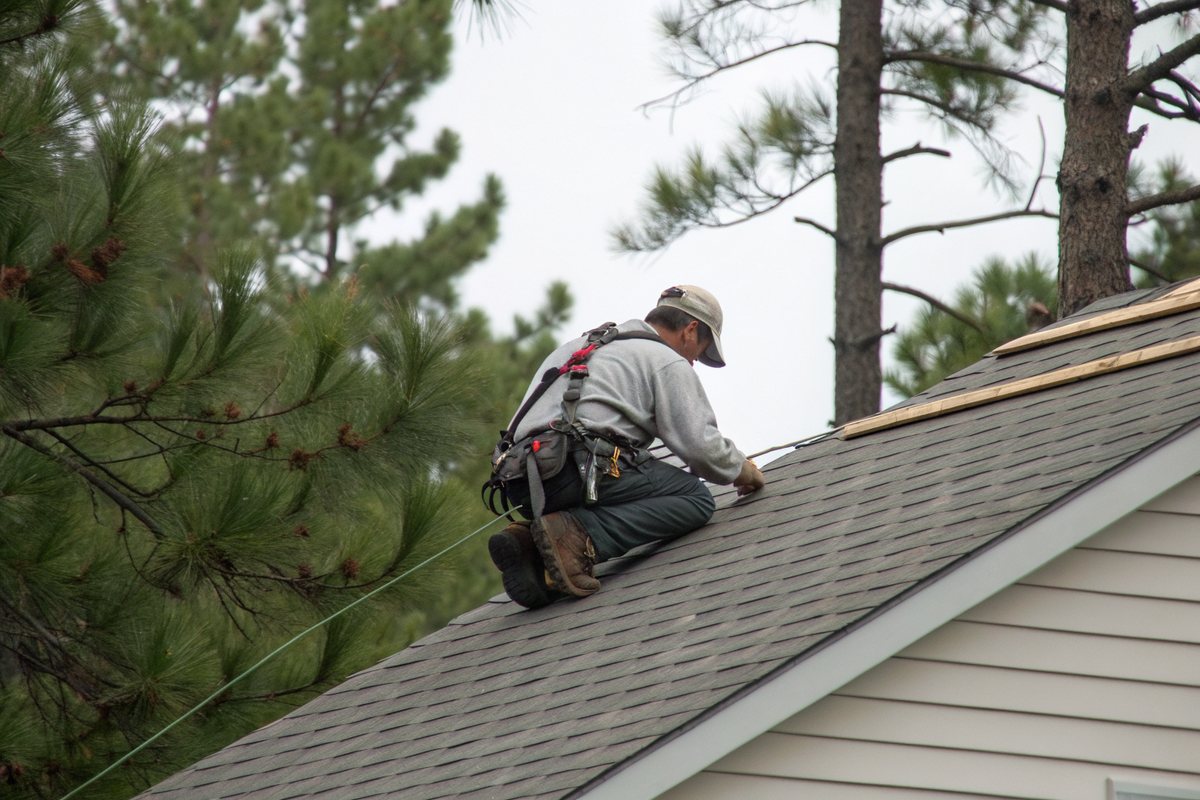 A roofer in a safety harness checking shingles on a house roof